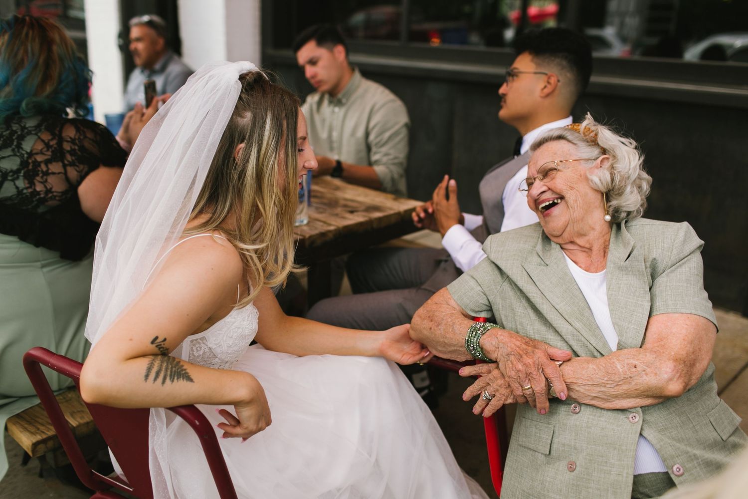 Bride in white dress shares a joyful moment with elderly woman in grey at outdoor reception.