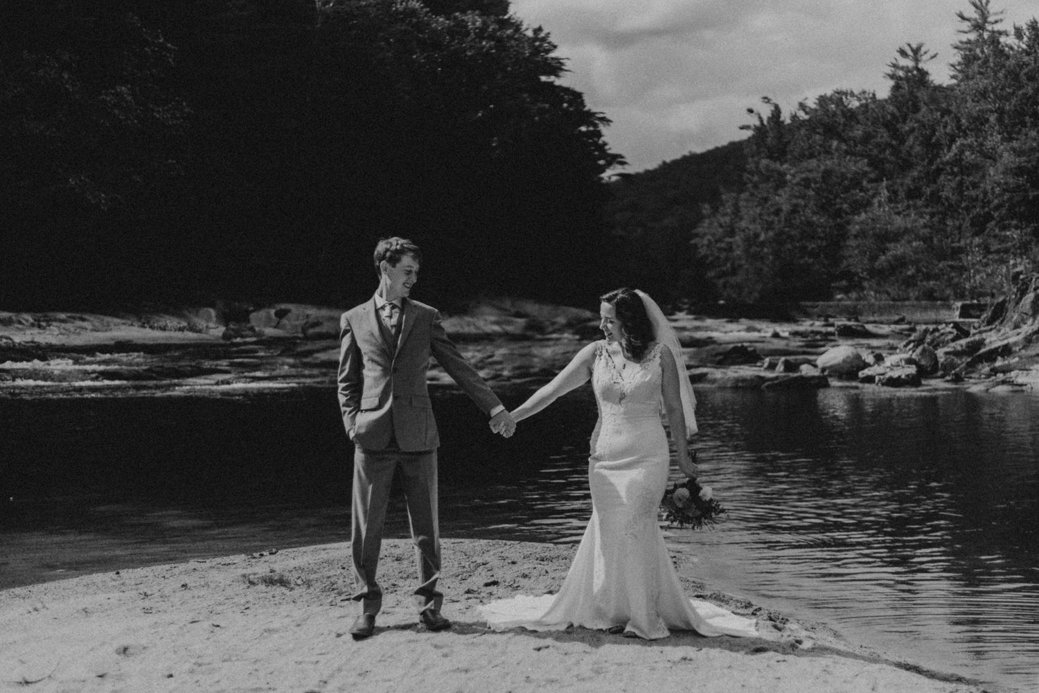 A couple celebrating their wedding day on a scenic riverbank in black and white.