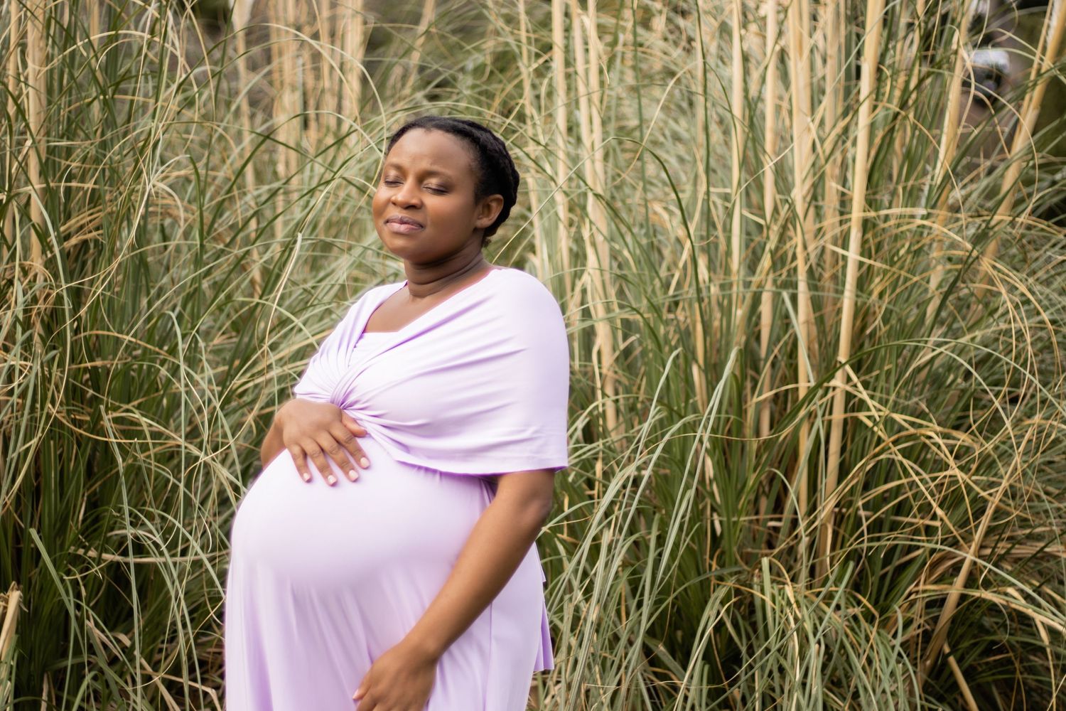 A pregnant woman holds her belly and closes her eyes, enjoying the sun