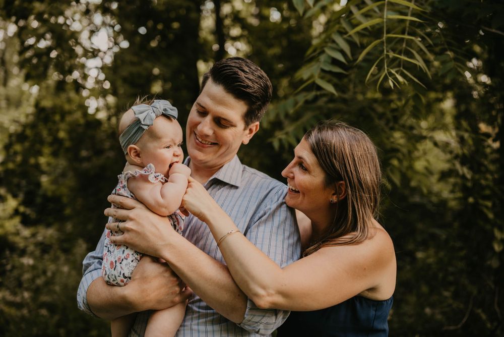 Loving parents smile at baby held up between them surrounded by tropical greenery.