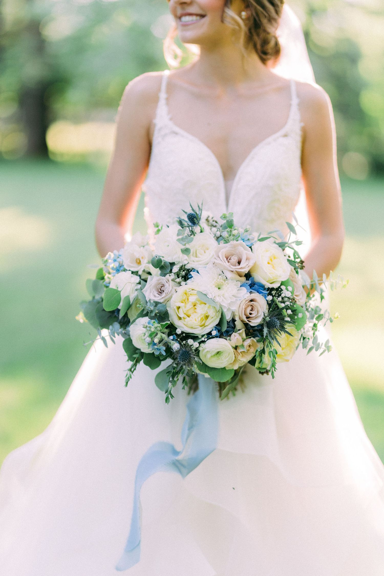 Romantic bridal bouquet featuring blush roses and blue ribbon against white wedding gown.