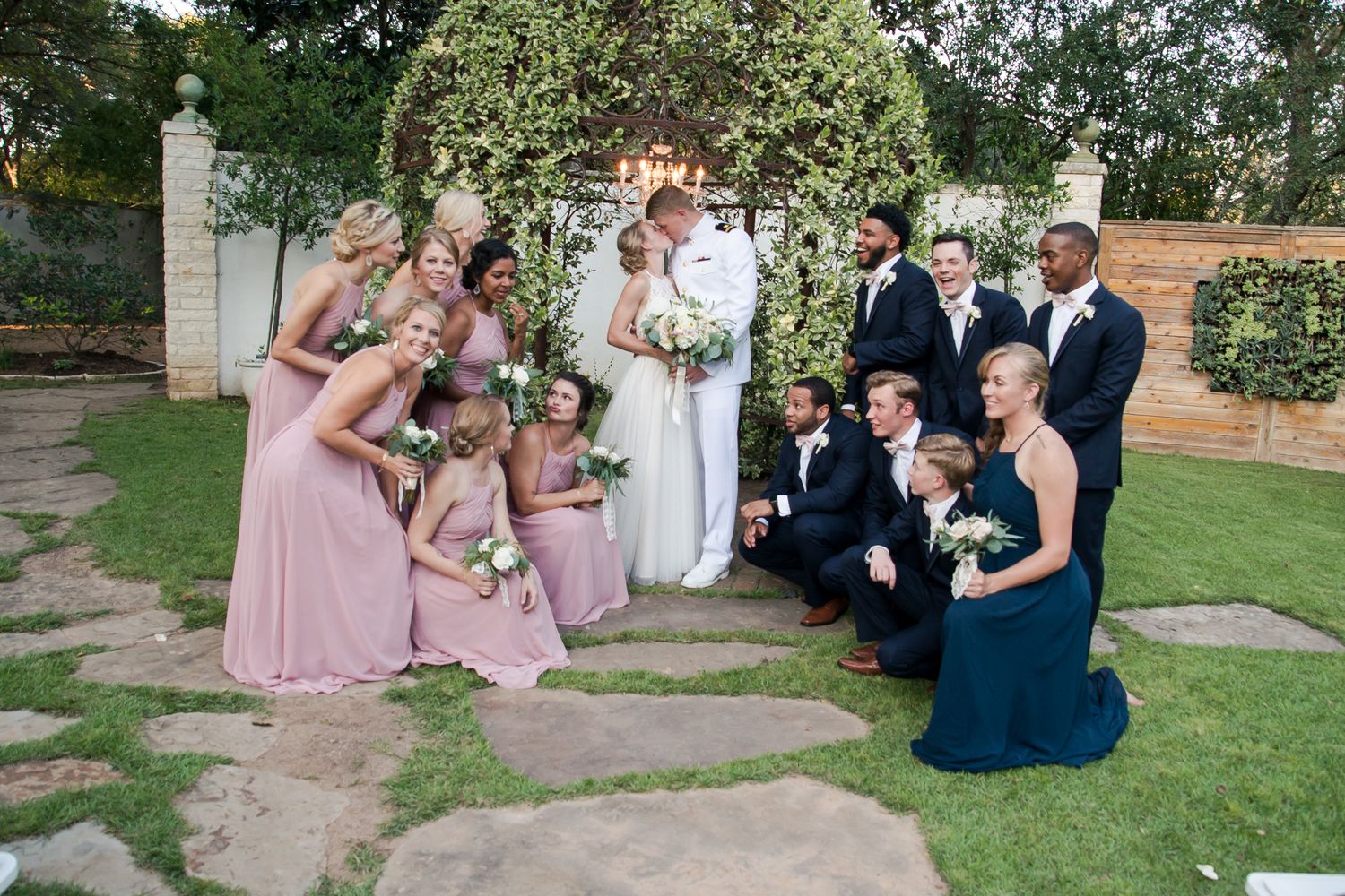 Wedding party poses casually on stone path during outdoor garden celebration.
