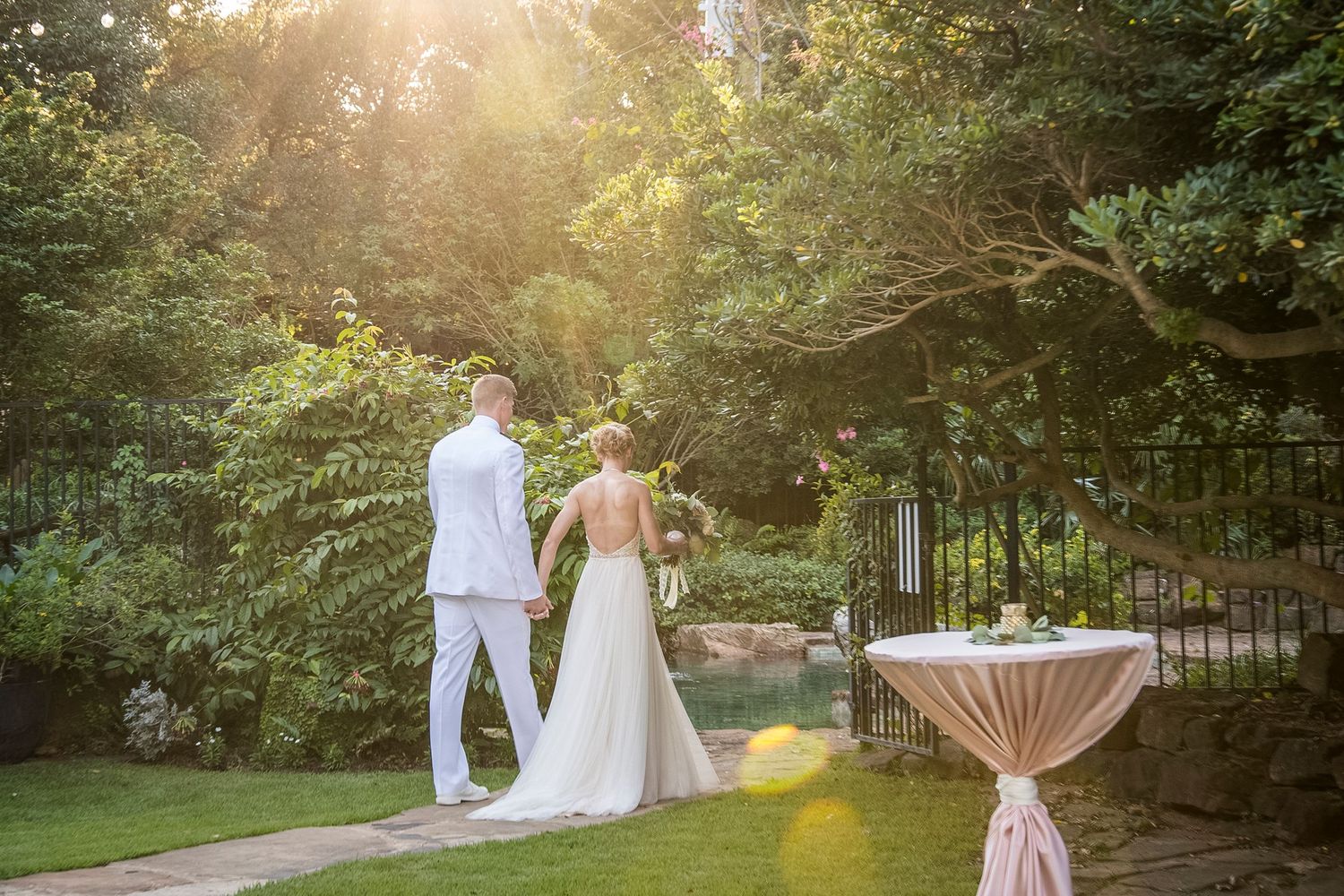 Couple strolls through garden at sunset with cocktail table in background.