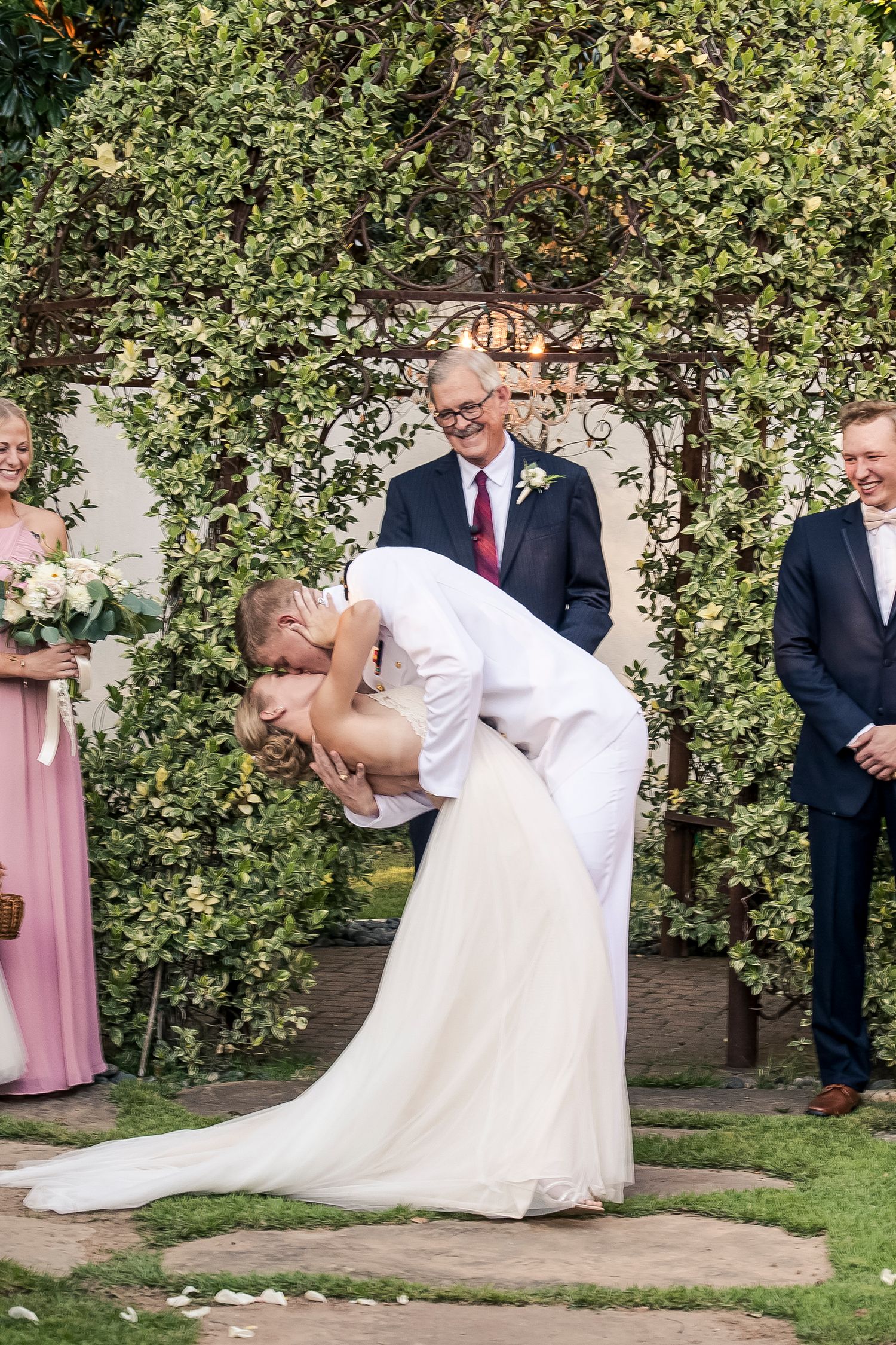 Romantic dip pose during garden wedding ceremony under floral archway.