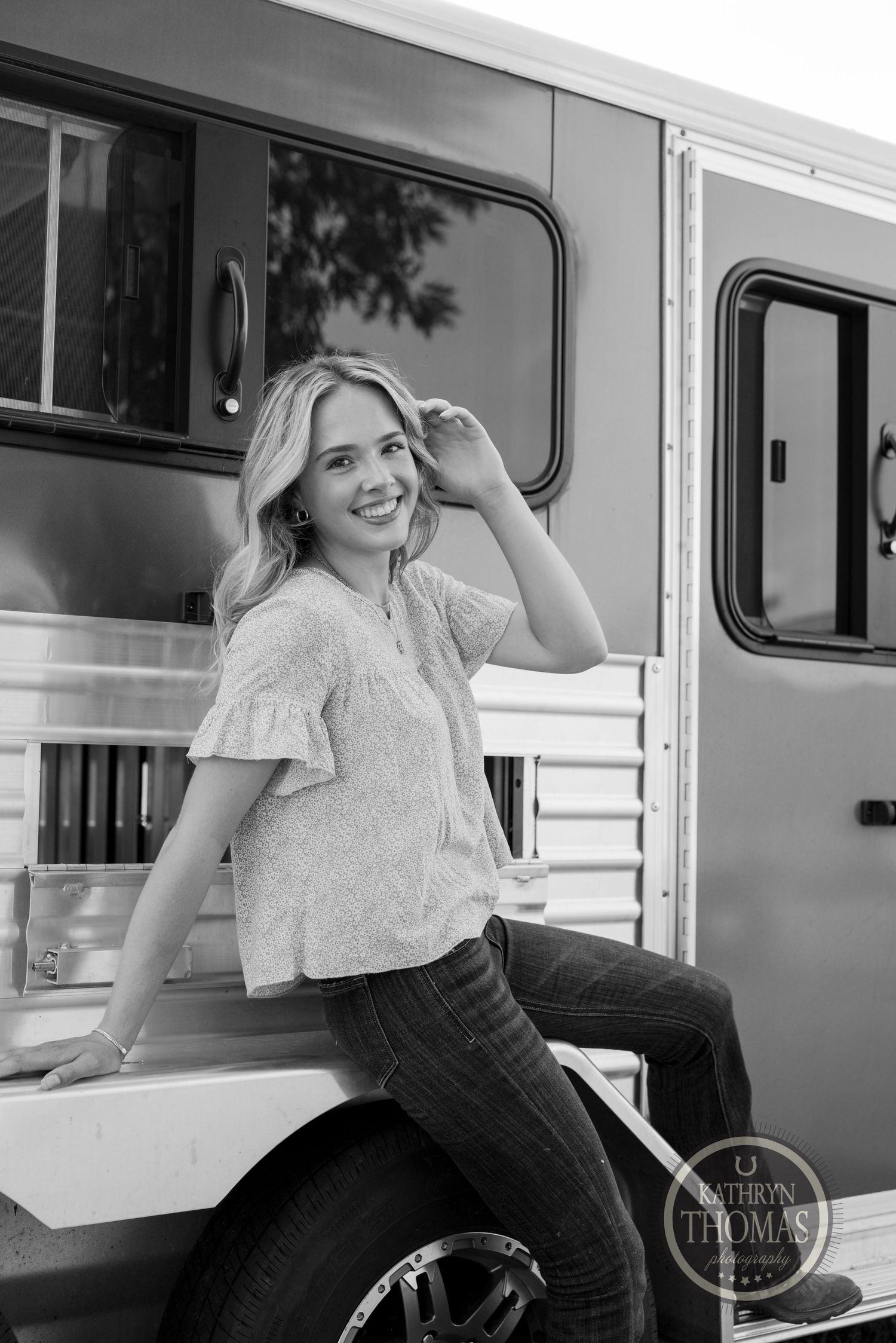 Someone leans against a silver horse trailer in casual attire.
