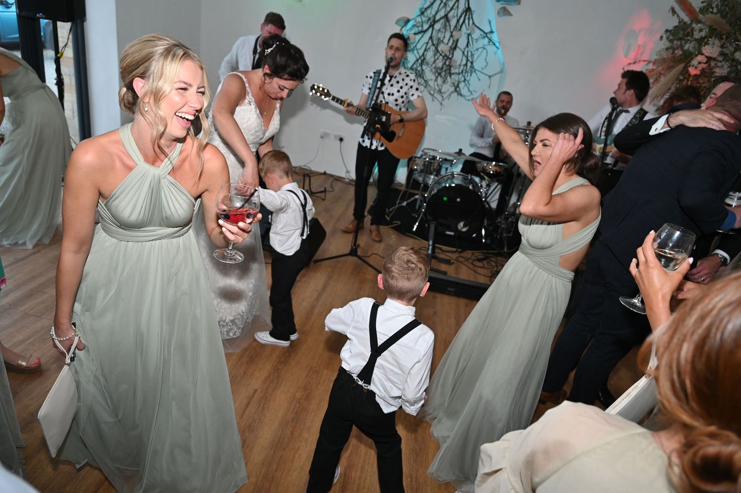 Wedding guests dancing and celebrating on a wooden dance floor under crystal chandeliers.