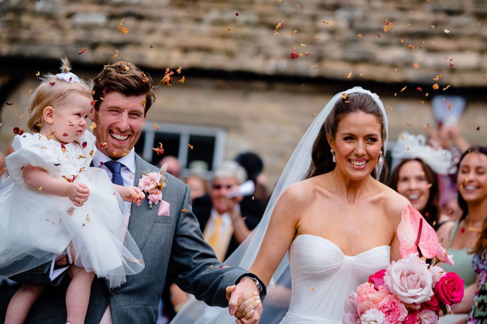 A wedding party celebrates with confetti outside on a sunny day.