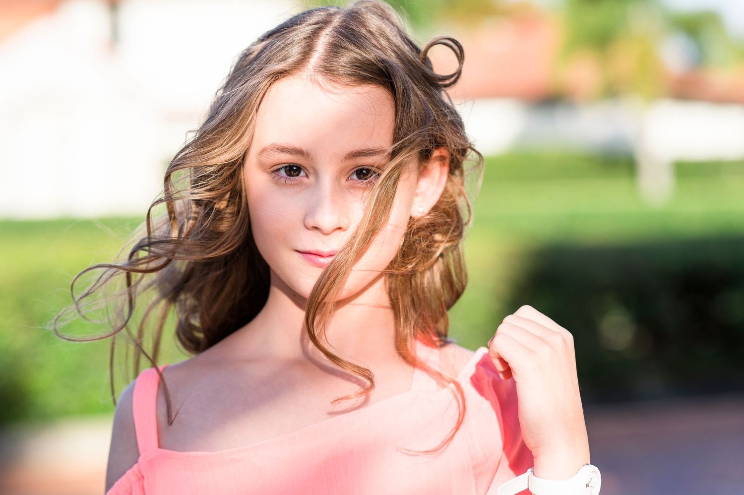 Outdoor portrait with windswept hair wearing coral colored top.