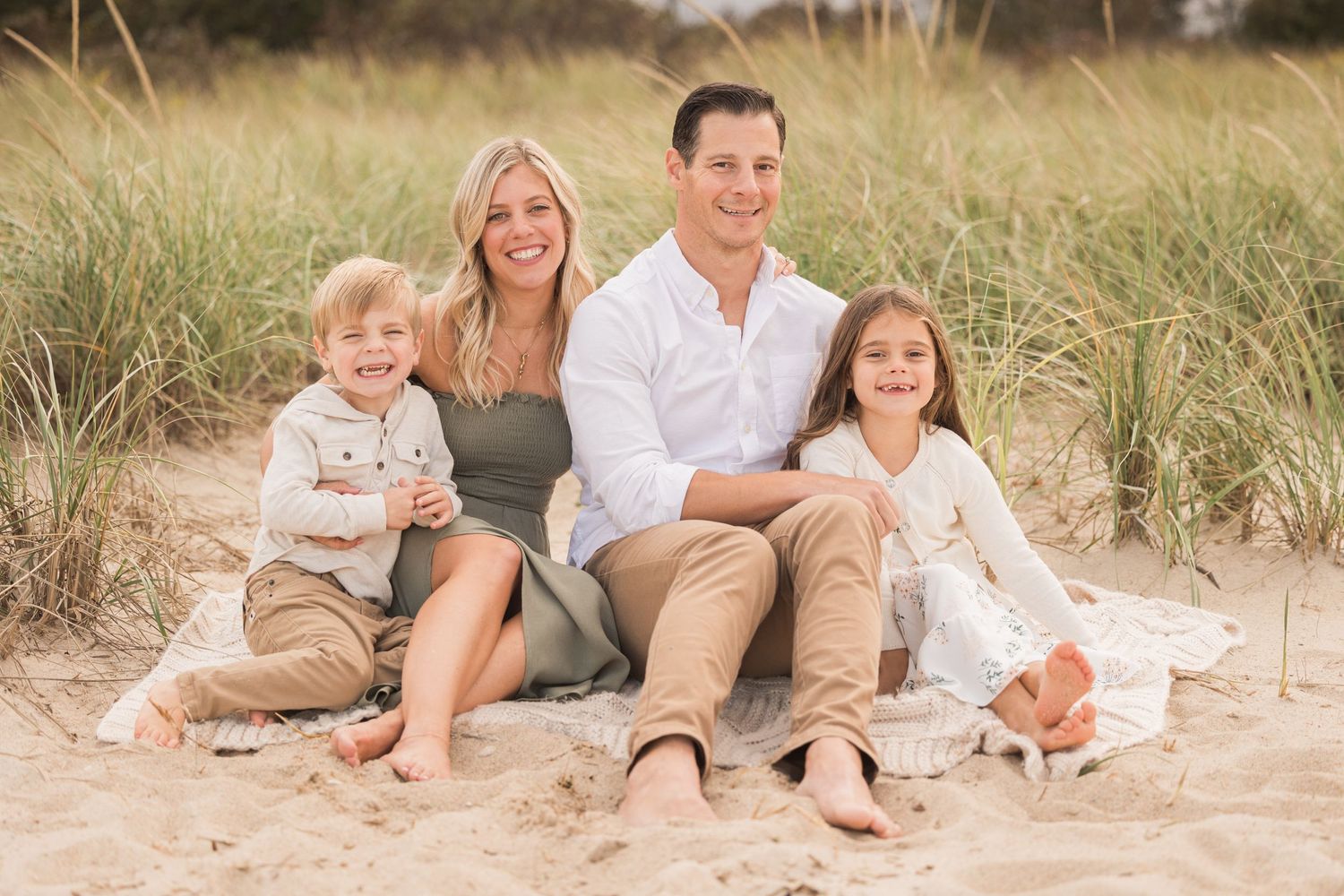 Happy family sitting together on sandy beach during sunset photo session.