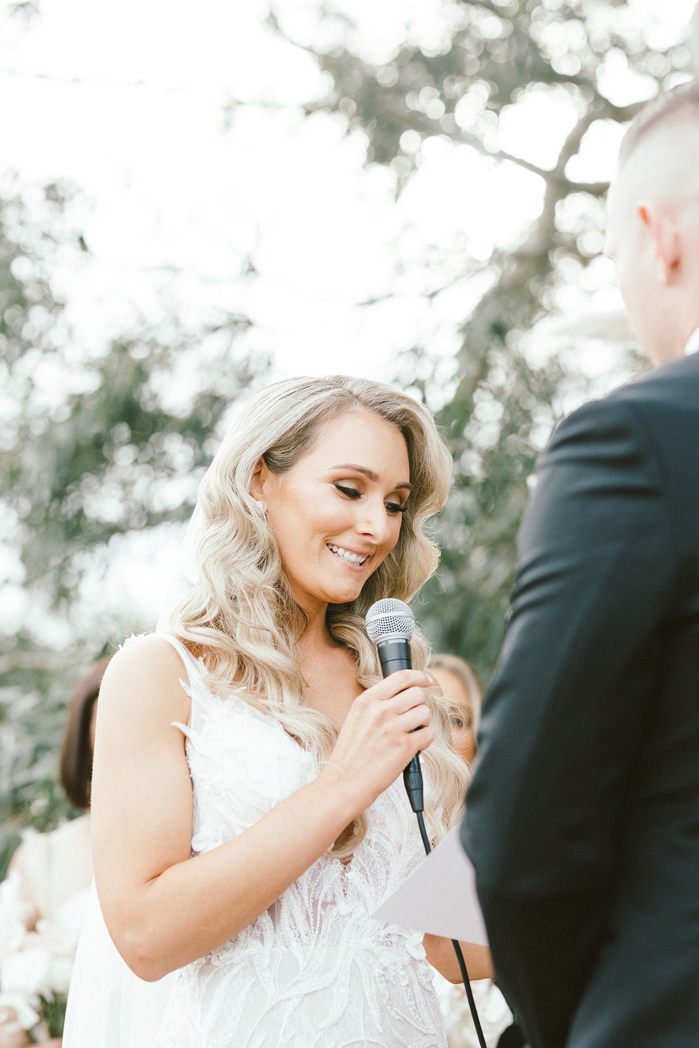 Wedding ceremony moment with microphone under willow trees.