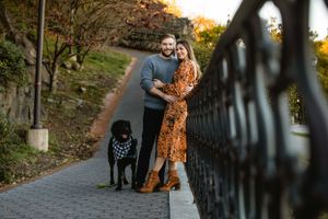 Couple and their black dog posing on pathway during autumn engagement session.