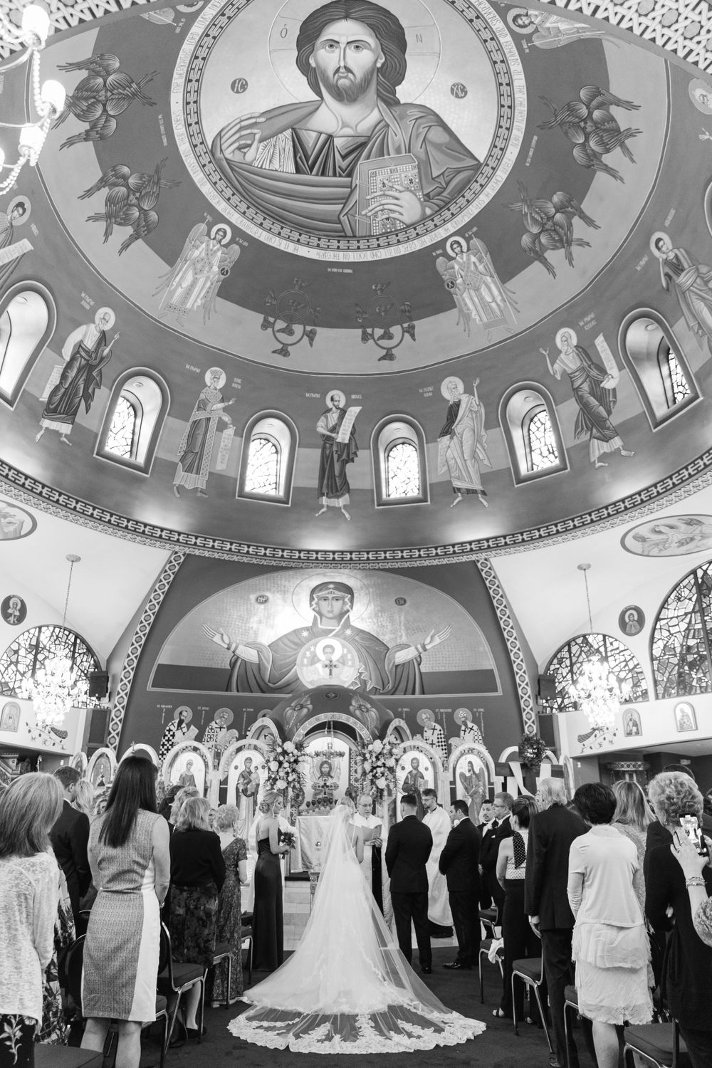 Wedding ceremony in Orthodox church with dramatic domed ceiling featuring religious iconography.