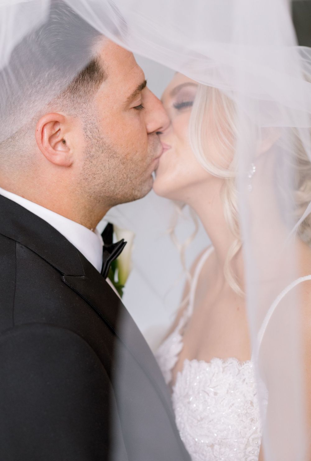 Romantic wedding kiss under delicate white veil.