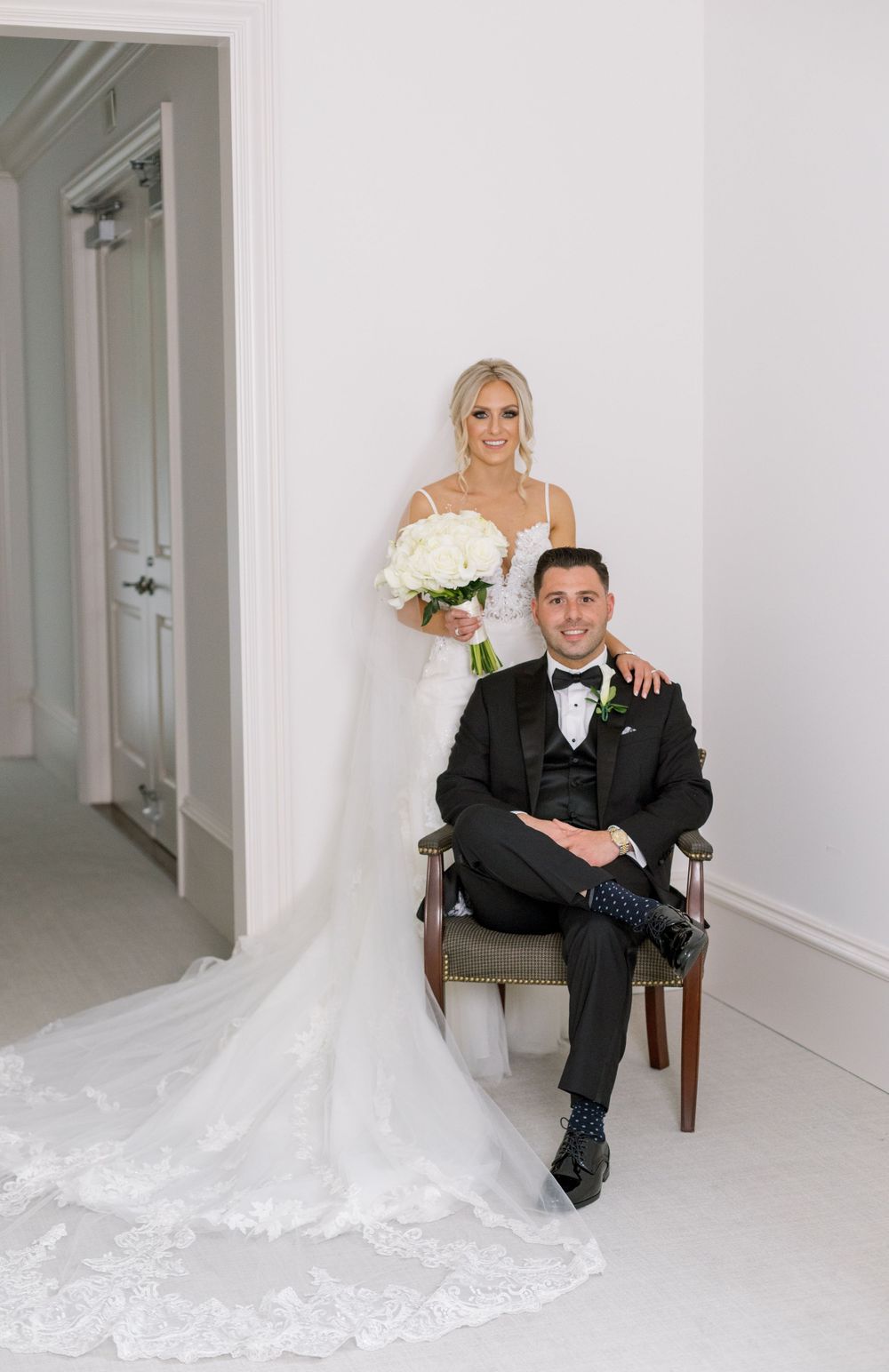Wedding portrait in minimalist white room with classic decor and elegant attire.