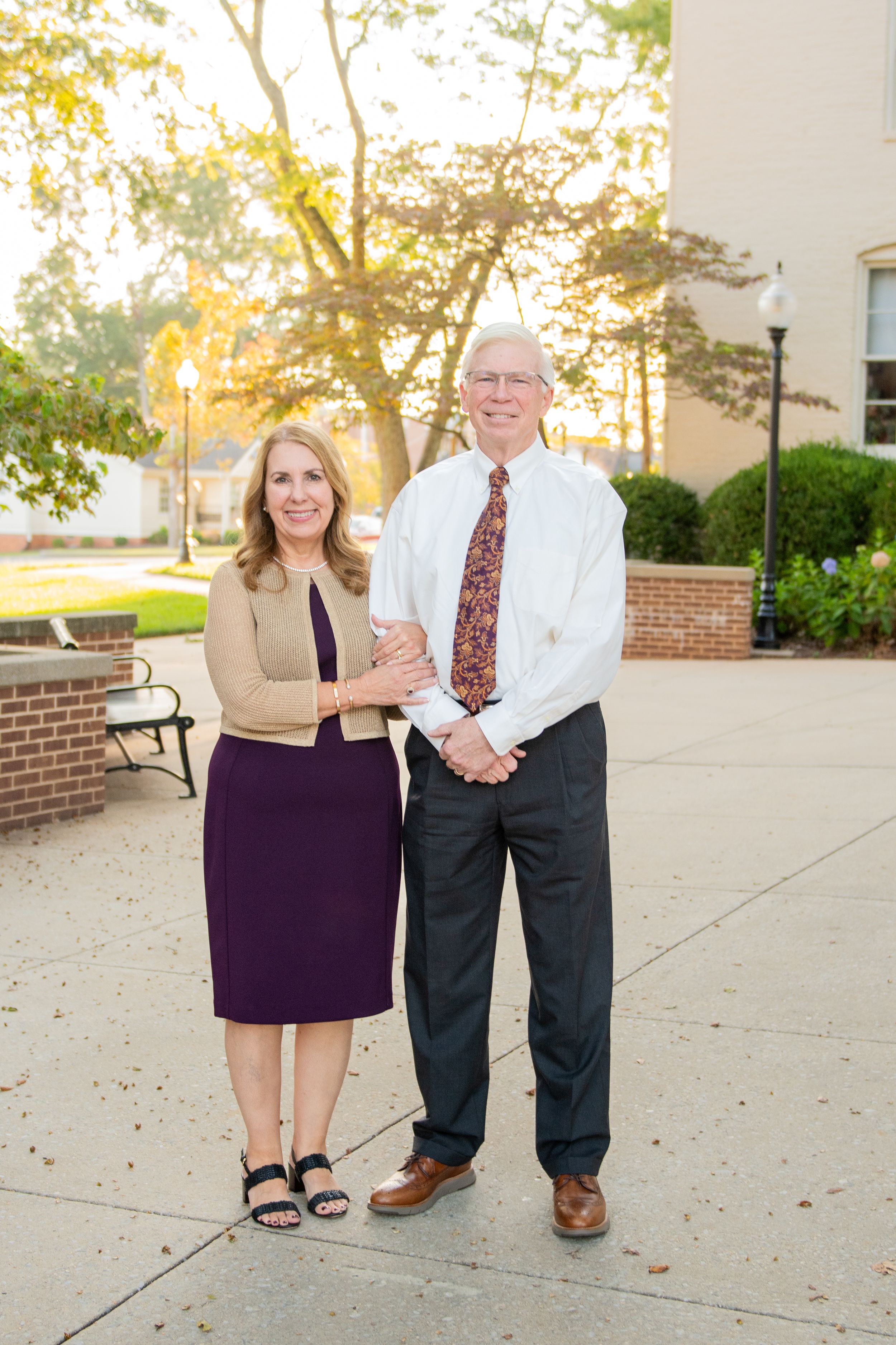 Couple poses together on concrete path during golden hour with brick building in background.