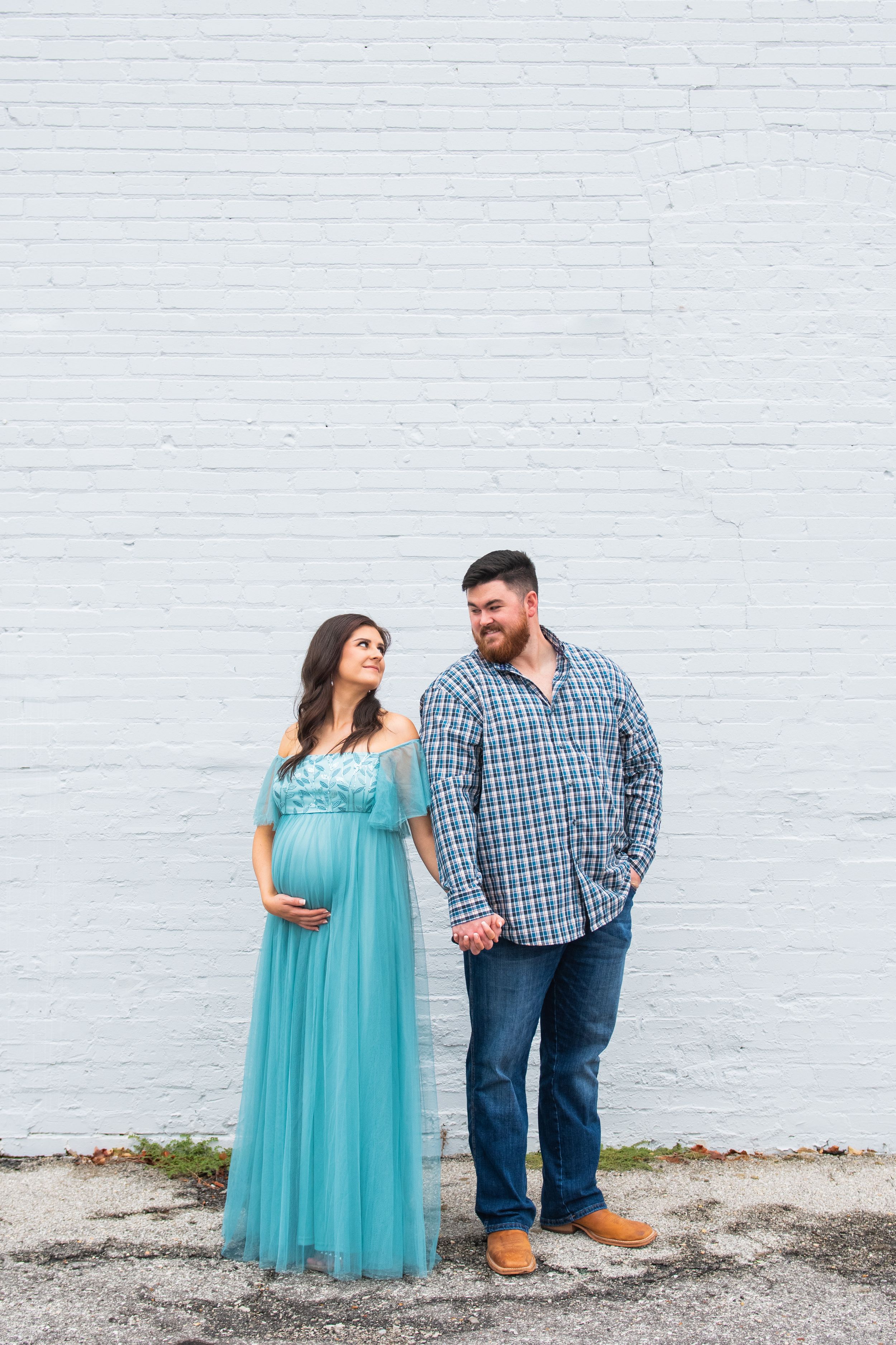 A couple shares a tender moment against a white brick wall background.