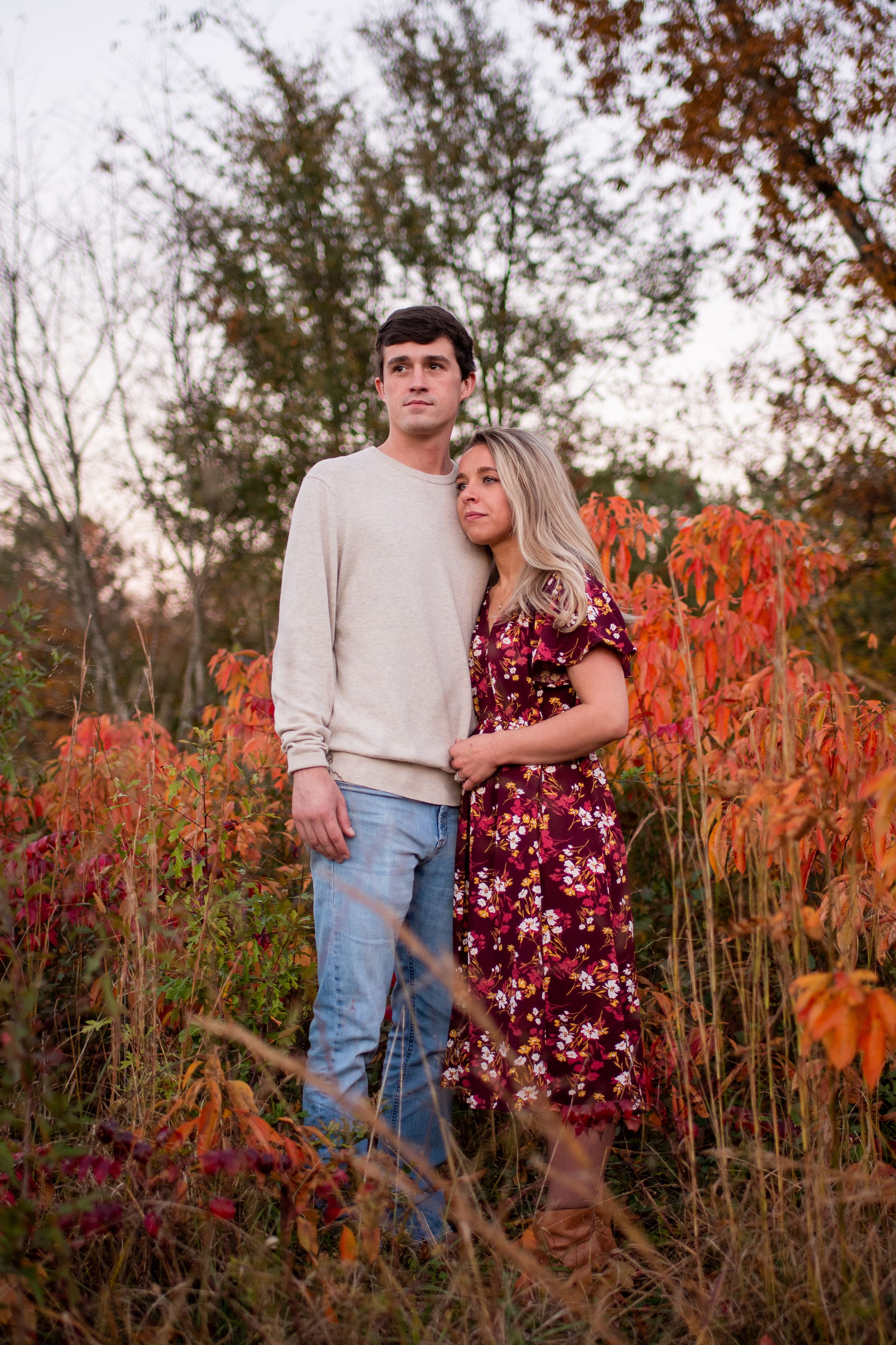 Romantic couple posing in field of red autumn flowers during golden hour.