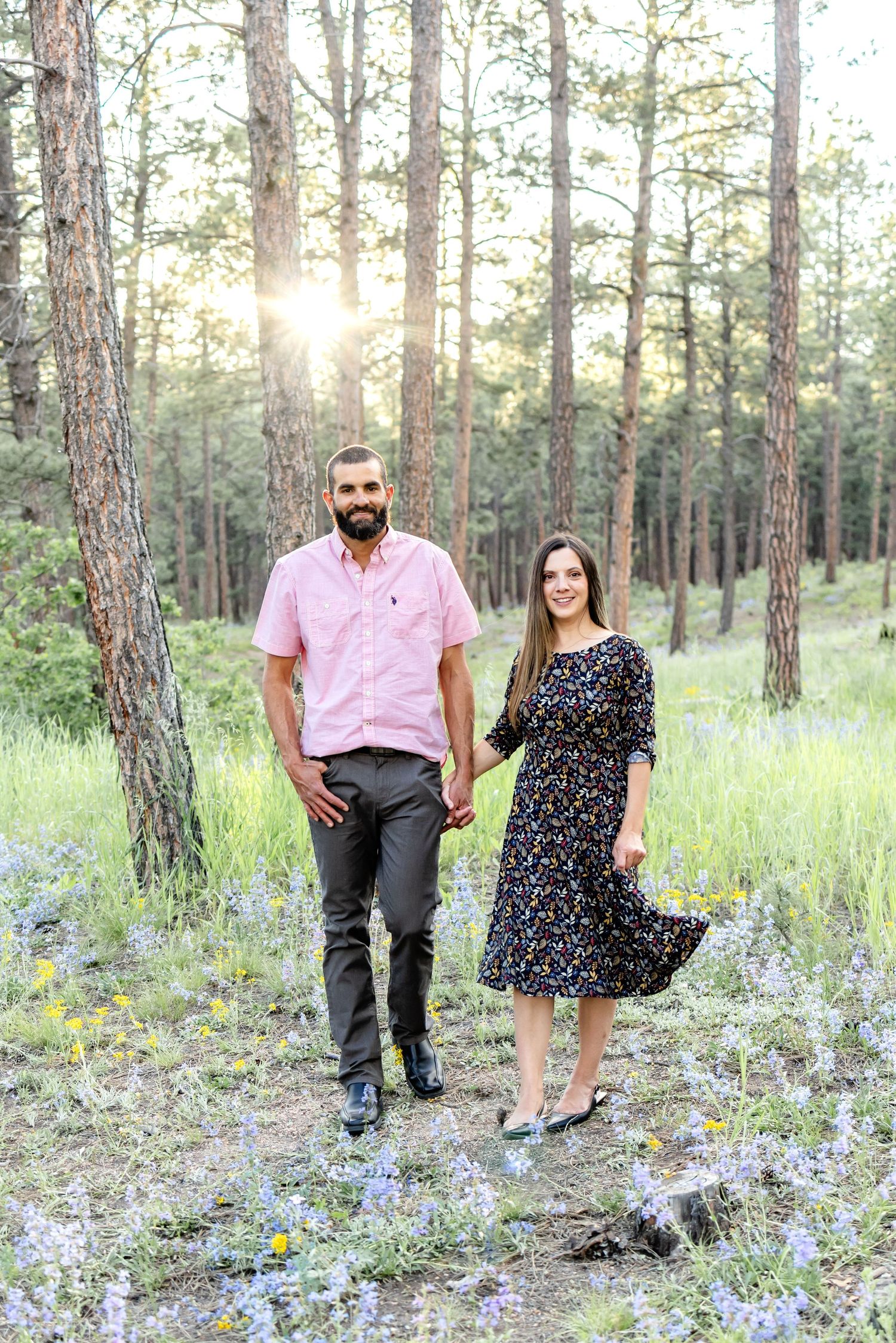 Husband and wife walk hand in hand through the forest at sunset during their family session in Colorado Springs.