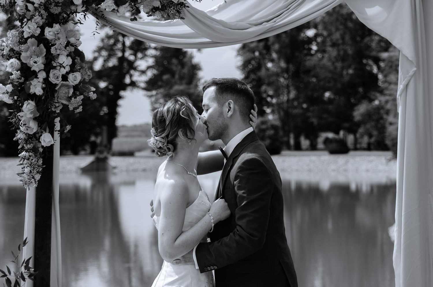 Wedding ceremony by lakeside gazebo decorated with flowing white fabric and floral arrangements.