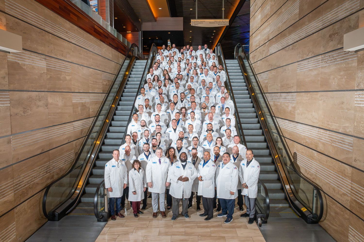 Large group photo of people in white attire gathered on modern architectural staircase.
