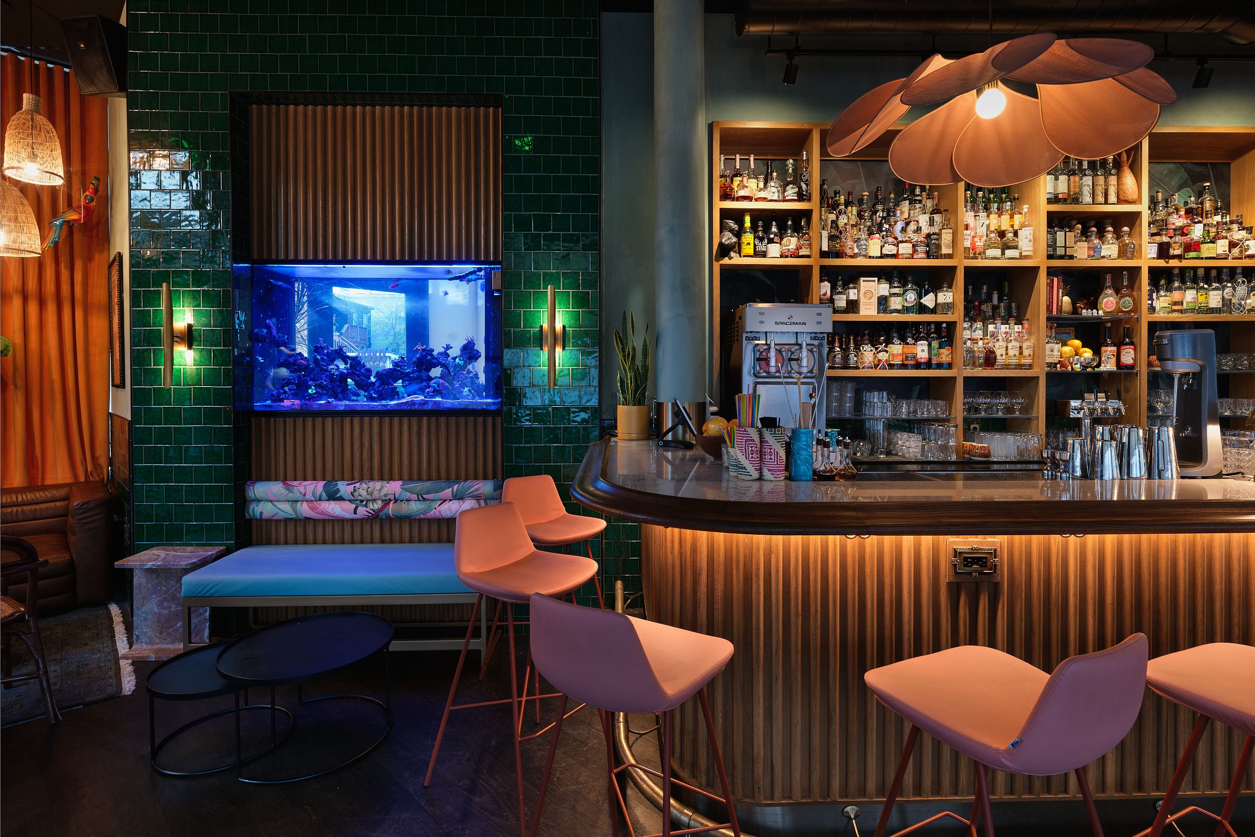 Stylish bar with green tiled walls, coral-colored chairs and a built-in aquarium display.