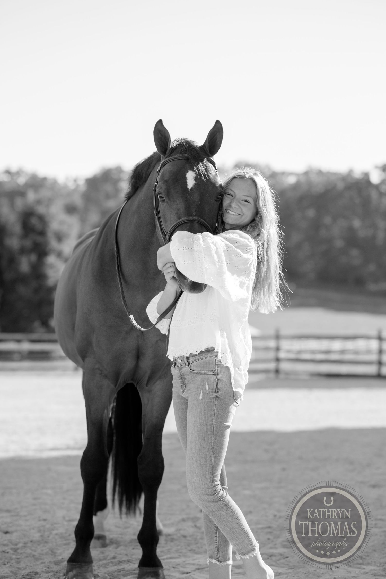 Black and white photo of person embracing horse in outdoor setting with fence visible.