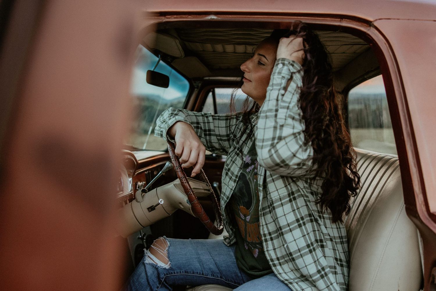 A woman in a flannel in the drivers seat of a ford f100 truck