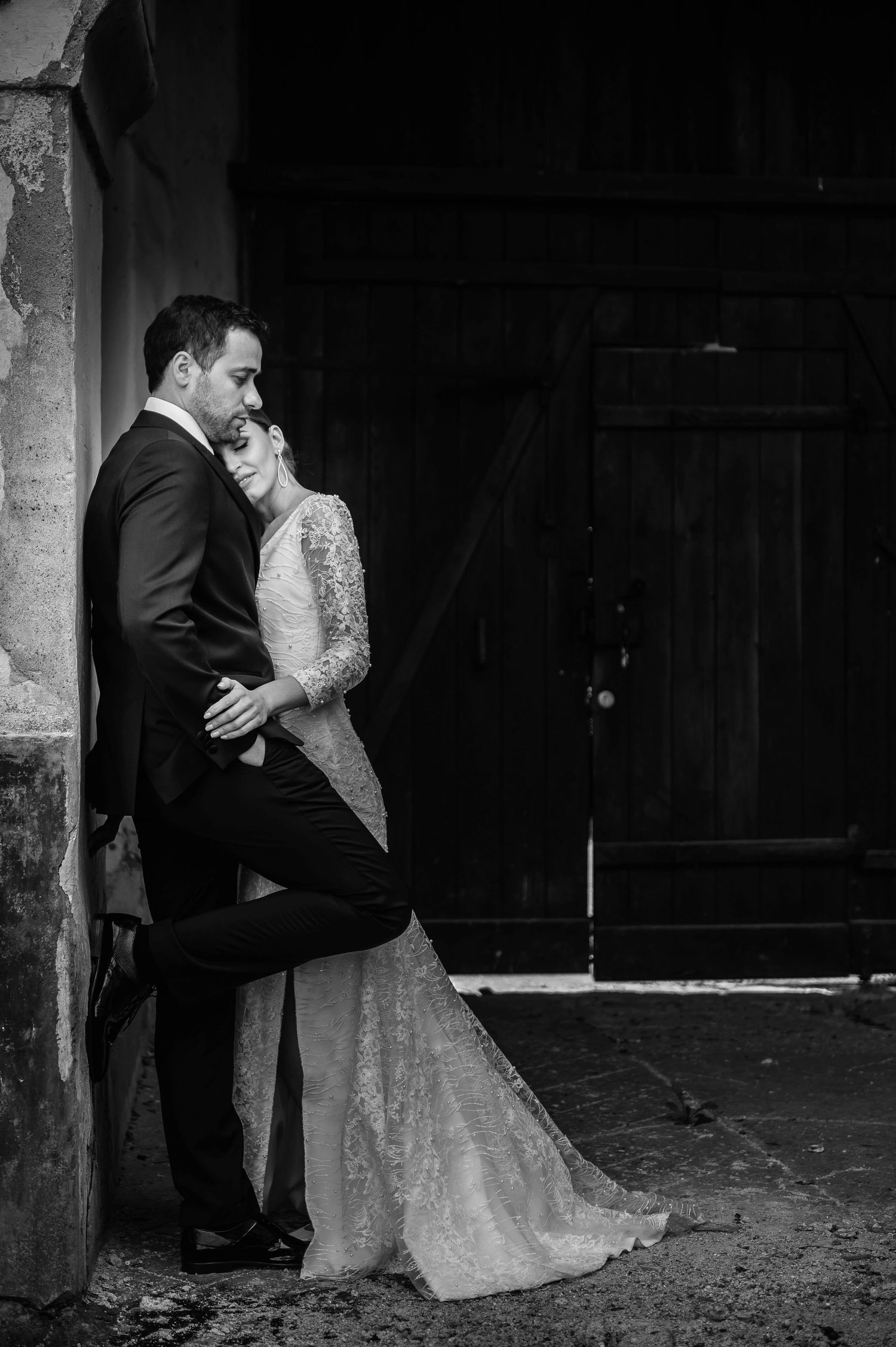 Romantic black and white wedding photo of a couple embracing against a rustic wall.