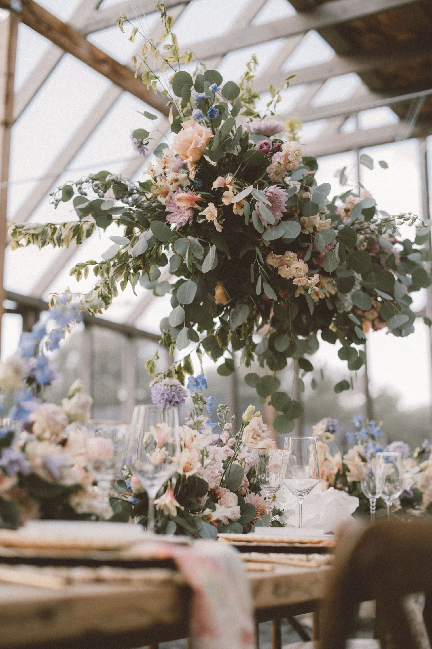 Dramatic floral chandelier with pink blooms and greenery above rustic dining table.