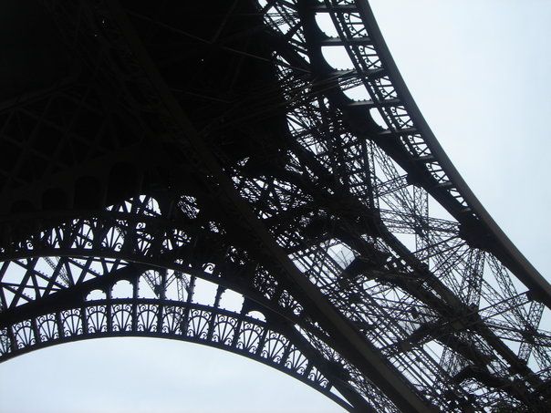Low angle black and white view of the Eiffel Tower iron lattice structure.