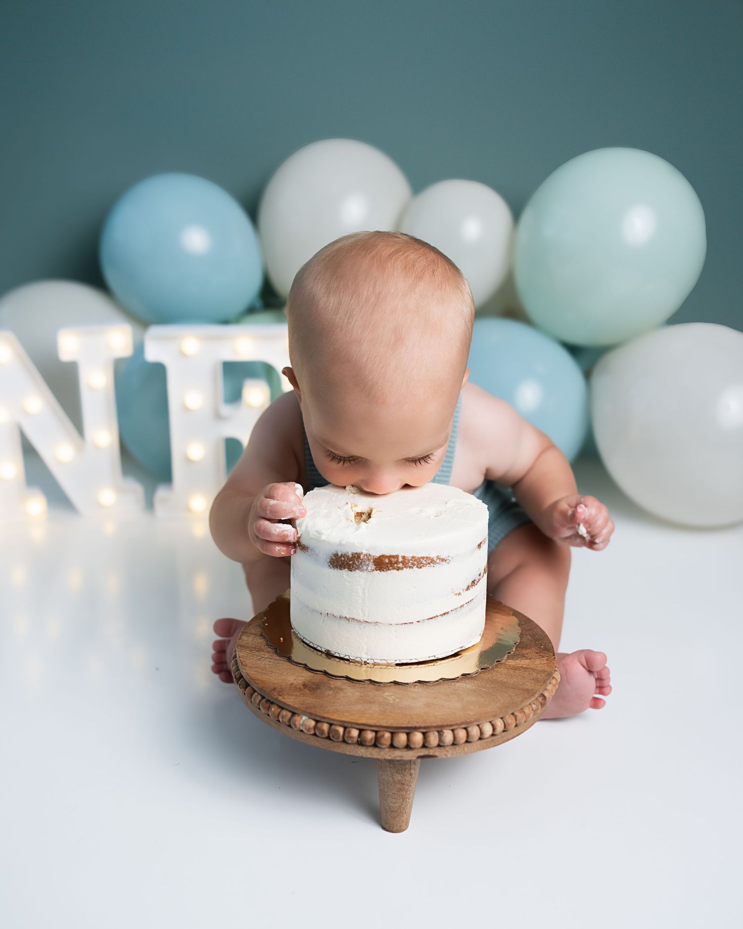Baby boy leans face-first into white birthday cake during first birthday cake smash photography session.