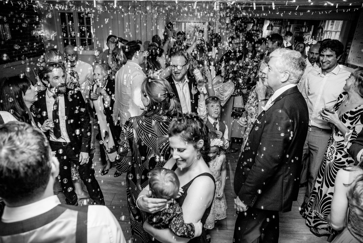 Black and white photo of wedding guests dancing amid a shower of bubbles.