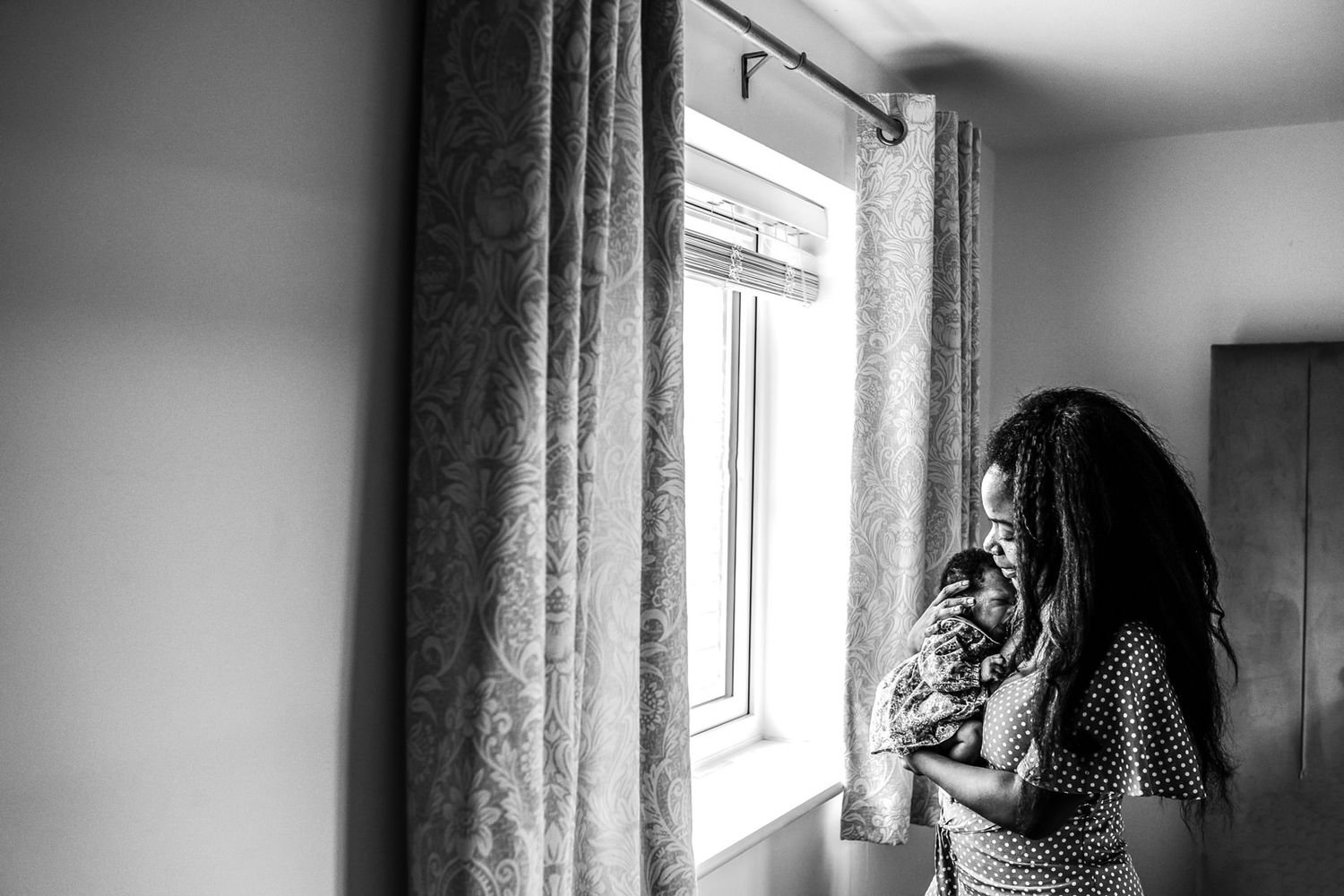Black and white, mother standing by window holding her newborn baby close