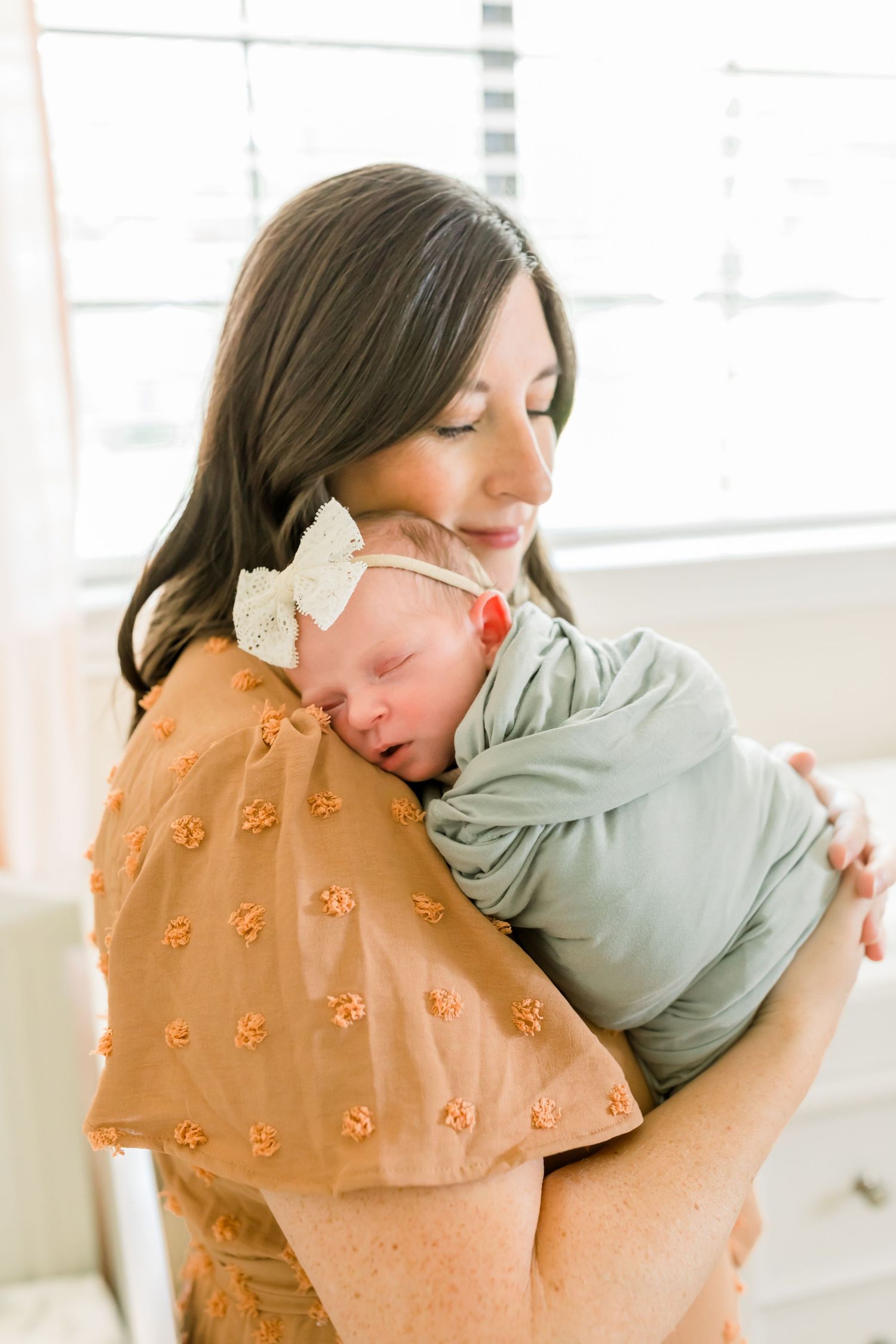 Tender moment in nursery as caregiver cuddles sleeping newborn wrapped in sage green swaddle.