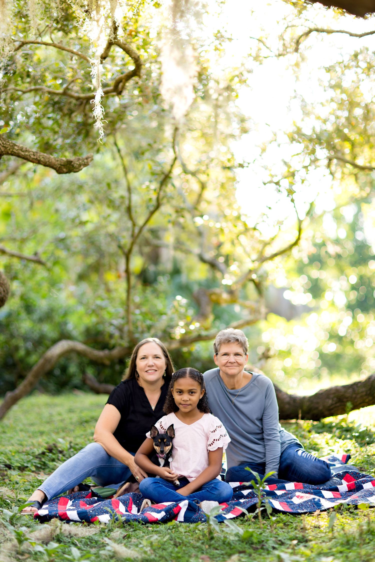 Family relaxing on a patriotic blanket under oak trees during sunset.