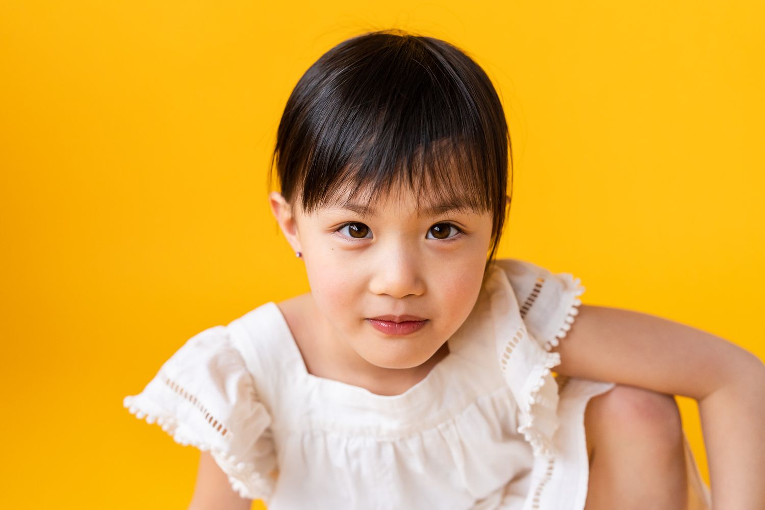 Portrait of a girl looking at the camera wearing a white dress in front of a yellow backdrop at a Seattle studio
