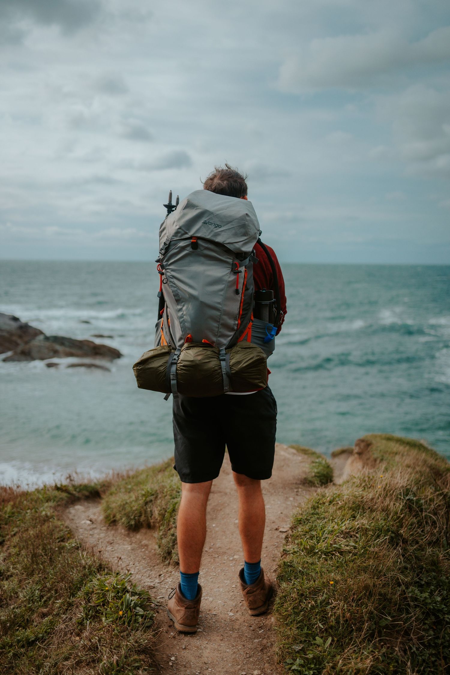 Back view of hiker with large backpack walking along coastal trail overlooking ocean.