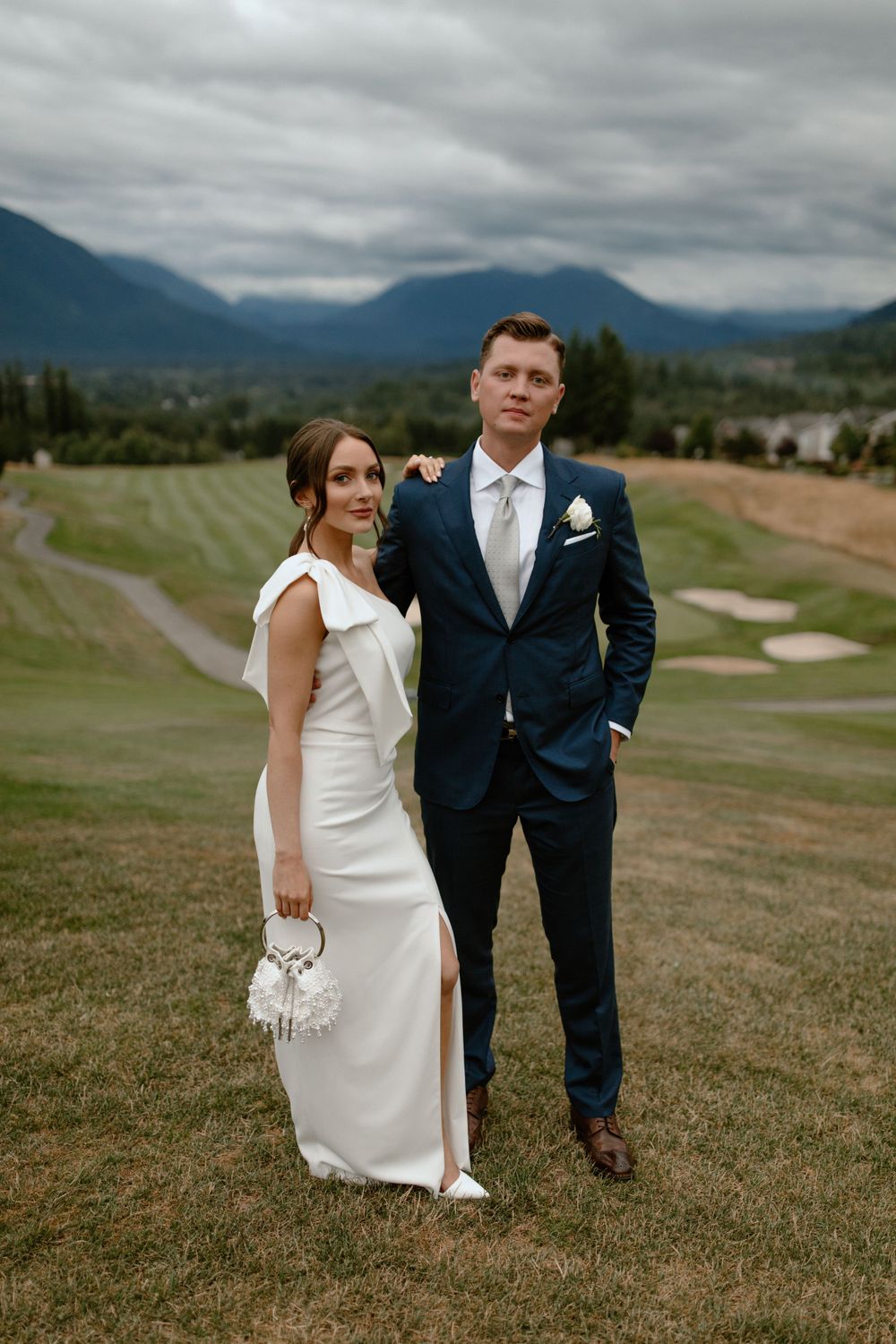 Wedding couple posing on a golf course with dramatic mountain backdrop.