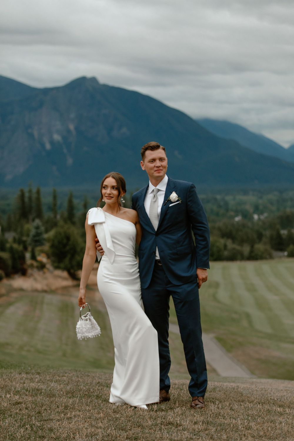 Wedding couple poses on golf course with mountain vista in background.