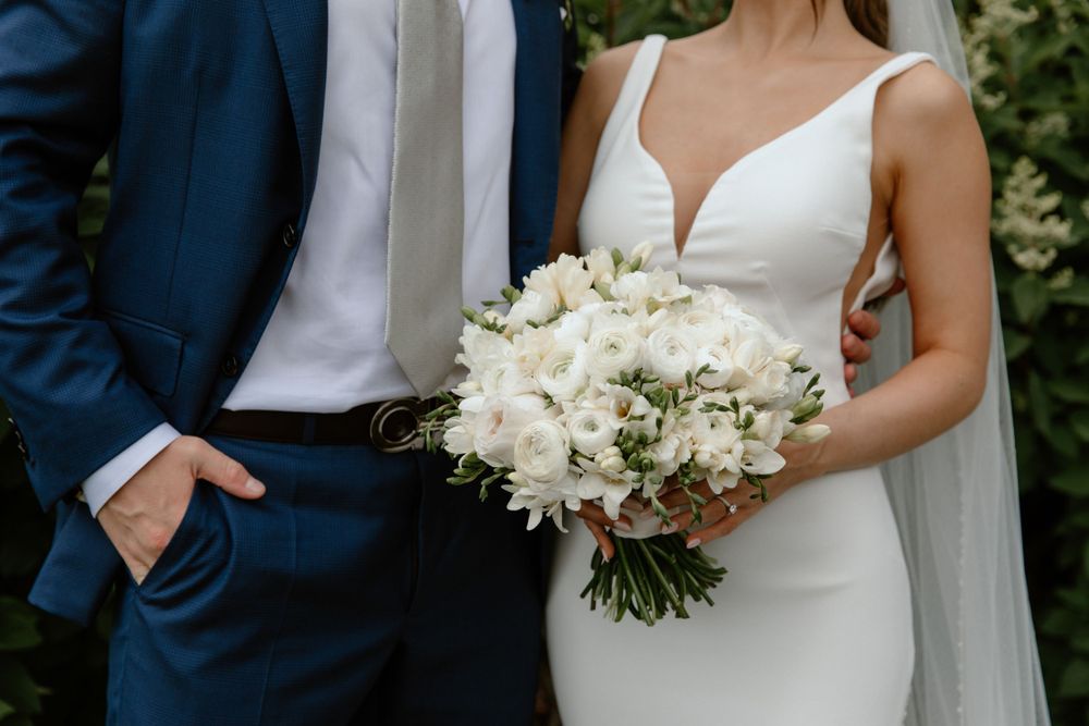 Elegant wedding details showing navy suit and white bouquet against natural backdrop.