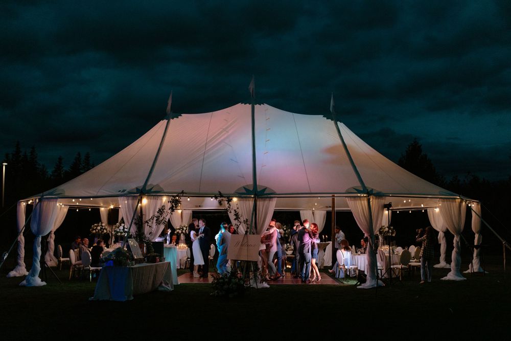 A large white wedding tent illuminated at night with guests mingling underneath.