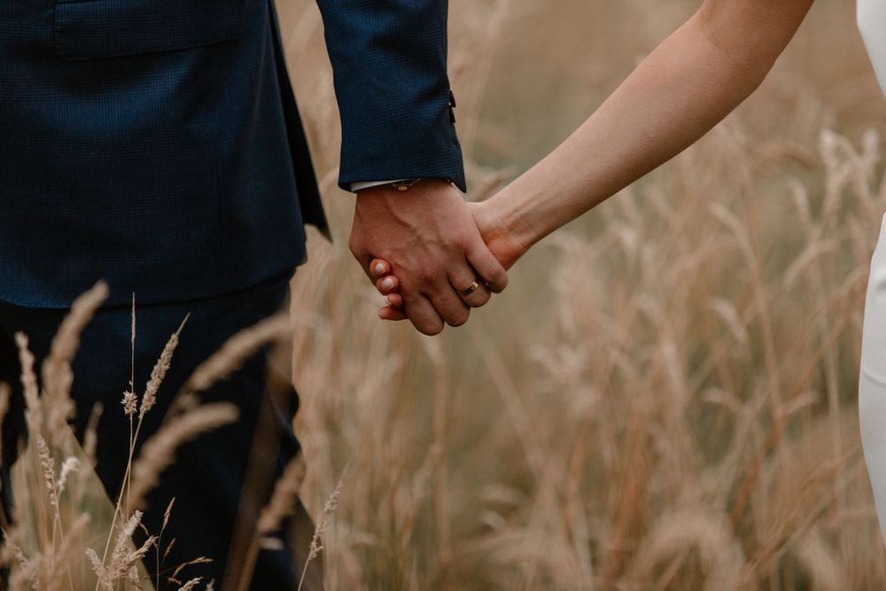 Close-up shot of a couple holding hands against a backdrop of golden wheat.