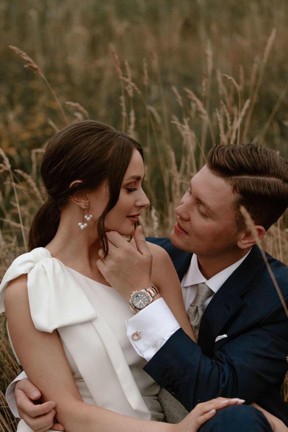 Intimate moment between newlyweds in a wheat field at sunset wearing formal wedding attire.