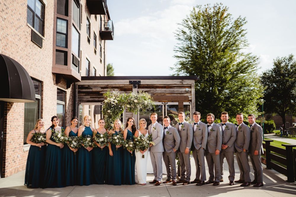 Wedding party poses outdoors with bridesmaids in teal and groomsmen in gray suits.