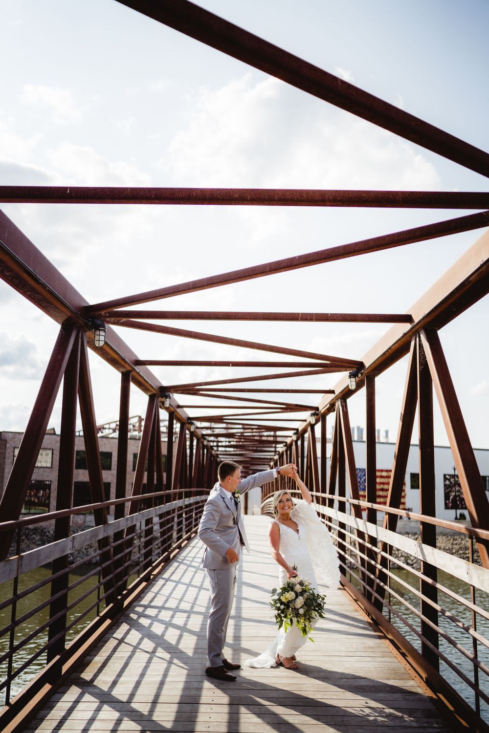 Wedding couple standing on rustic metal bridge with geometric architectural framing.