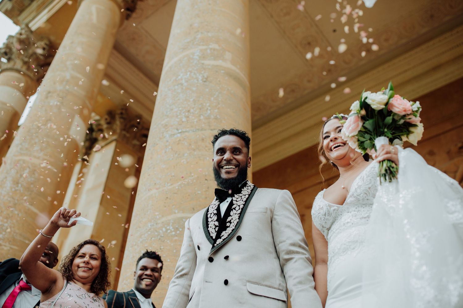 Wedding celebration outside historic building with confetti and classic columns.