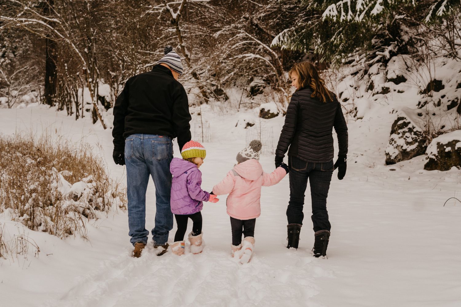 Family walking together through snowy winter forest path.