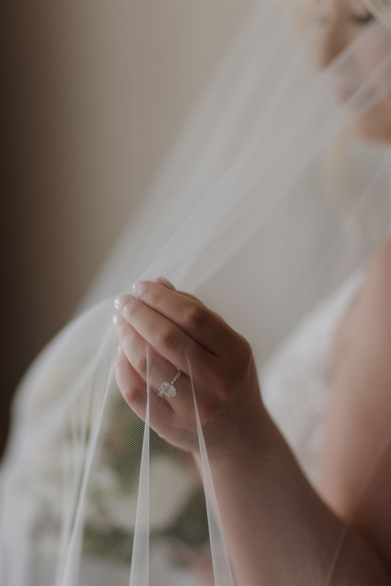 Close-up detail of a hand holding sheer wedding veil with engagement ring visible.