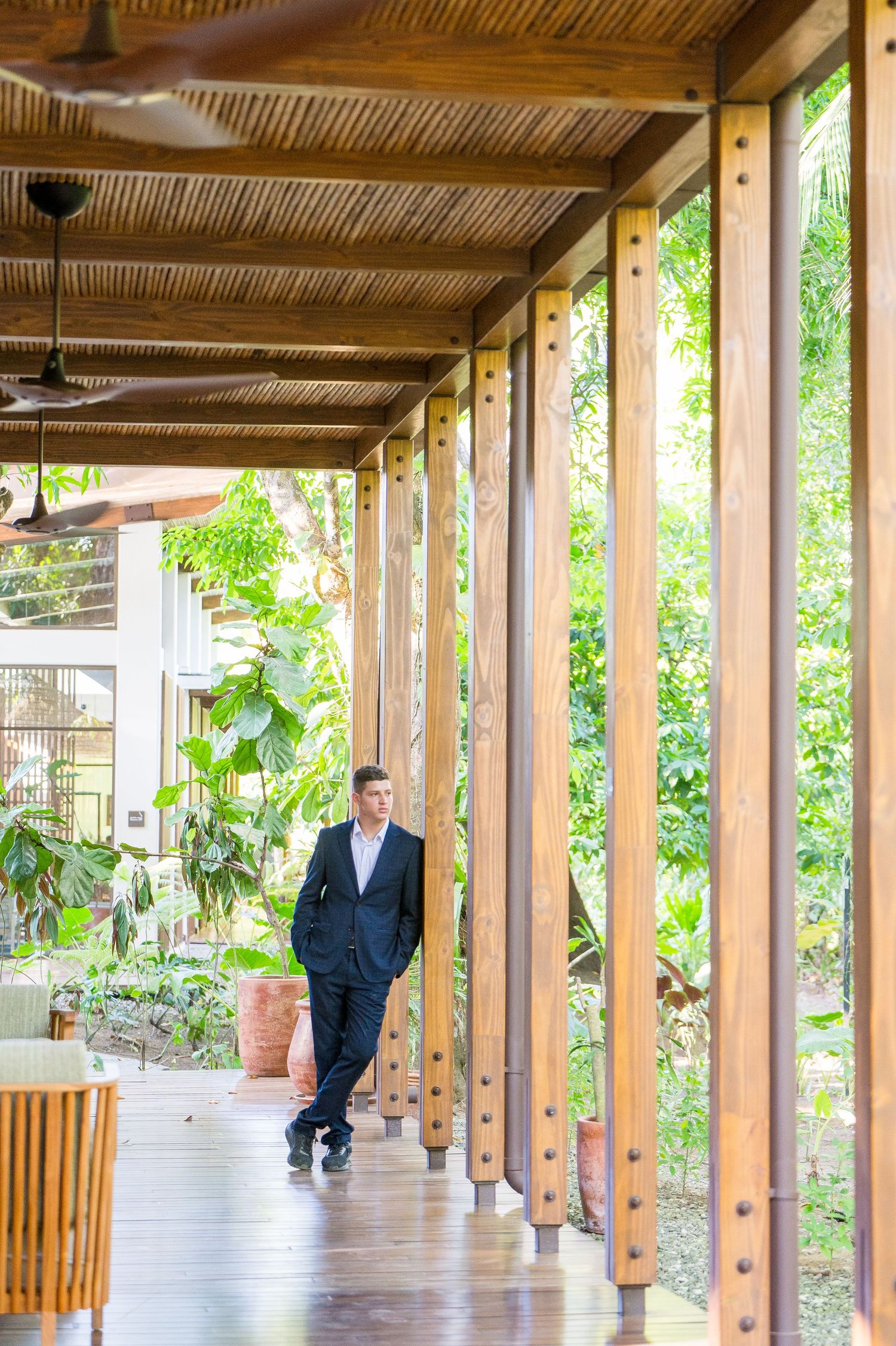 Groom leaning on wooden columns, contemplating the greenery of the courtyard.