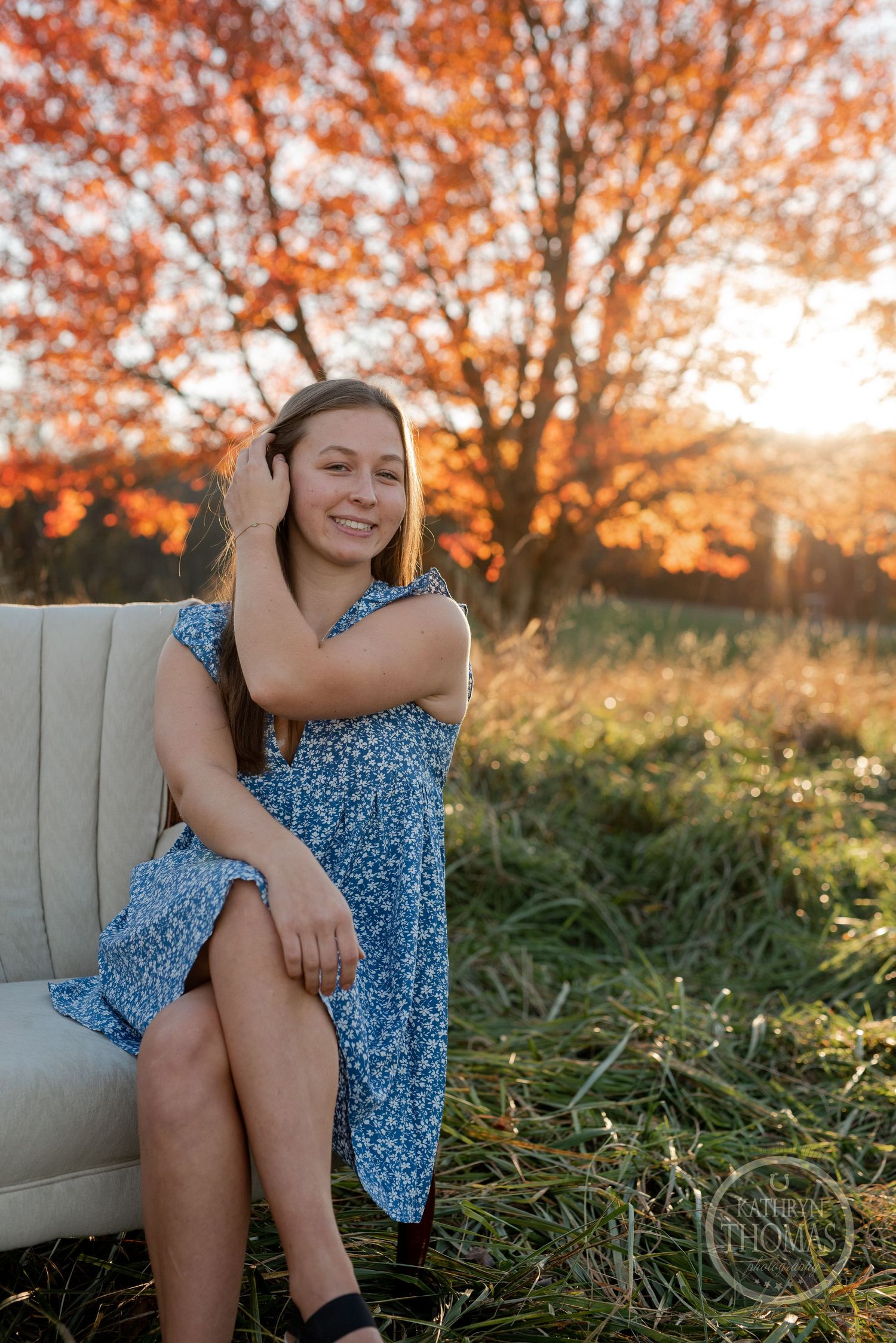 A blue dress on a beige armchair with orange fall foliage and sunset lighting.